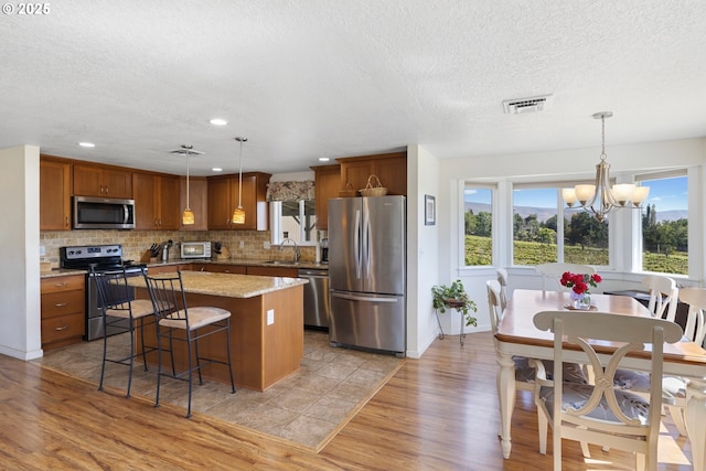 5073 Chenoweth Rd, The Dalles, OR 97058 - kitchen with appliances with stainless steel finishes, a sink, light wood finished floors, brown cabinets, and a textured ceiling