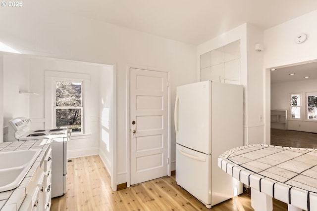 kitchen with sink, white appliances, light hardwood / wood-style flooring, white cabinetry, and tile countertops