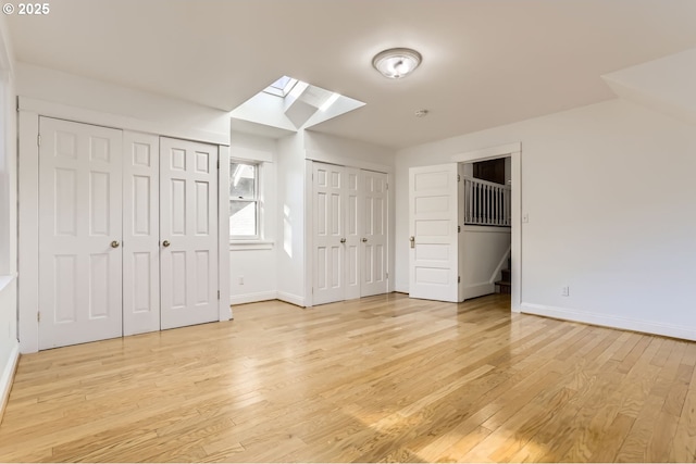 unfurnished bedroom featuring a skylight, light hardwood / wood-style flooring, and two closets