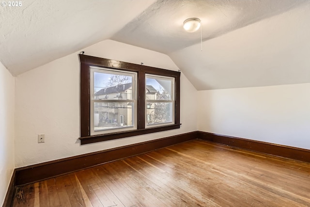 additional living space with wood-type flooring, a textured ceiling, and vaulted ceiling