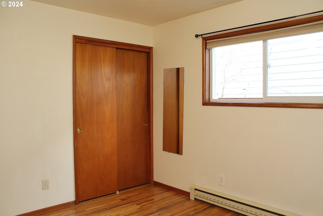 unfurnished bedroom featuring a baseboard radiator, a closet, light wood-style flooring, and baseboards