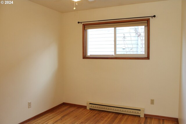 empty room featuring baseboard heating, light wood-style flooring, baseboards, and a ceiling fan