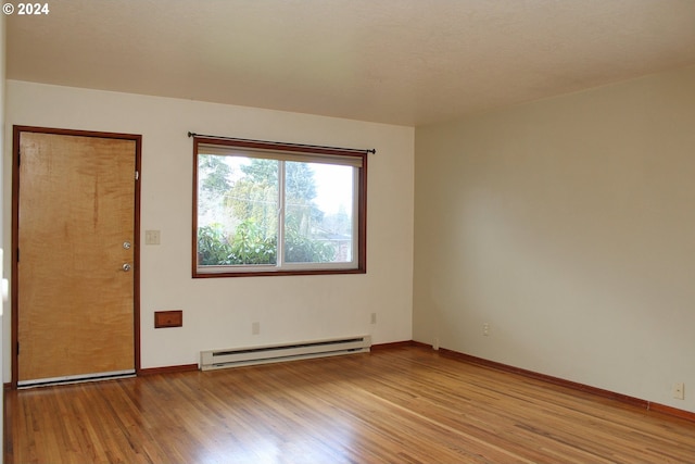 spare room with a baseboard radiator, light wood-type flooring, and baseboards