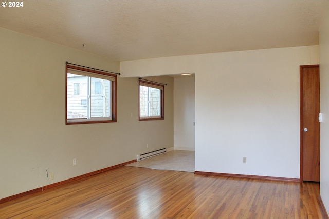 empty room with baseboard heating, light wood-style floors, and baseboards