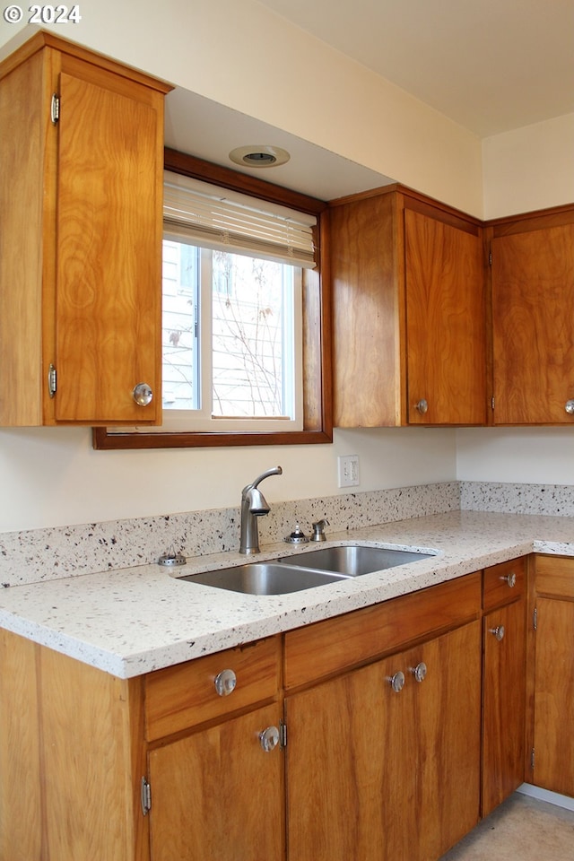 kitchen featuring a sink, brown cabinetry, and light stone counters