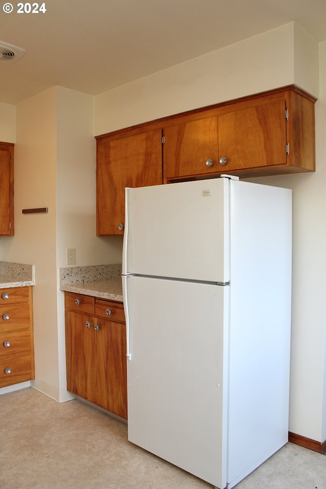 kitchen featuring freestanding refrigerator, brown cabinets, and light stone counters