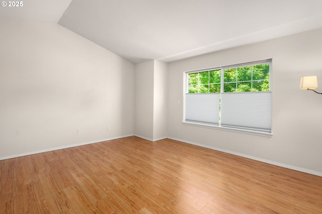 empty room with lofted ceiling, light wood-style flooring, and baseboards