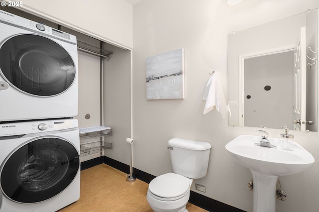 half bathroom featuring stacked washer / dryer, toilet, and baseboards