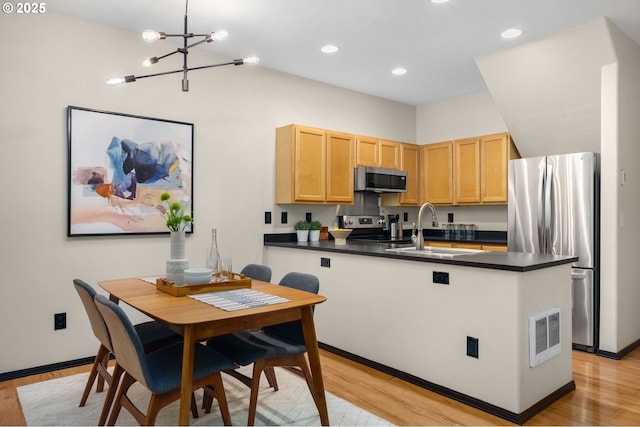 kitchen featuring stainless steel appliances, a sink, dark countertops, light brown cabinetry, and a peninsula