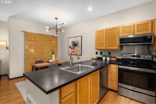 kitchen with appliances with stainless steel finishes, a sink, a peninsula, dark countertops, and a chandelier