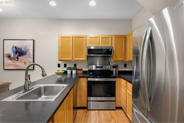 kitchen featuring appliances with stainless steel finishes, a sink, dark countertops, recessed lighting, and light wood finished floors
