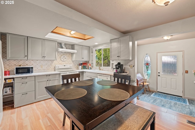 kitchen featuring tasteful backsplash, white appliances, light countertops, light wood-style floors, and a sink