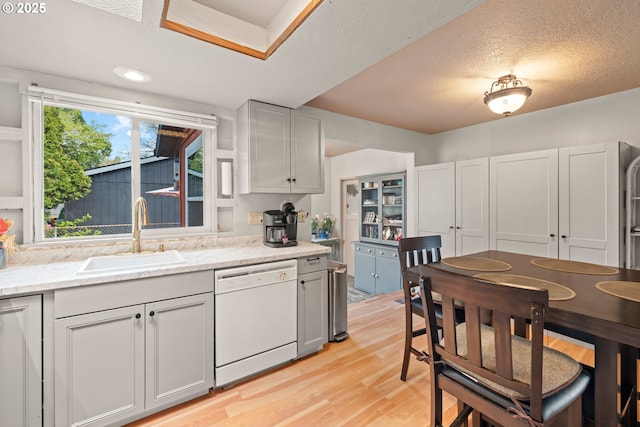 kitchen featuring light wood-style floors, light stone countertops, a textured ceiling, a sink, and white dishwasher