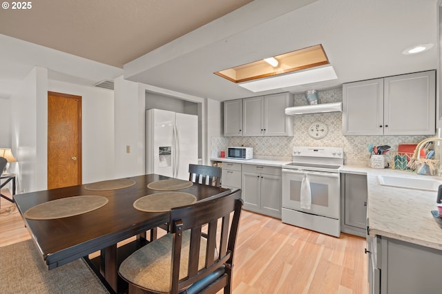 kitchen with a sink, gray cabinets, white appliances, and light wood-style floors