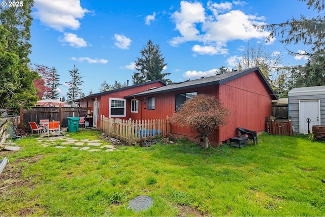 rear view of house featuring a shed, an outdoor structure, fence, and a lawn