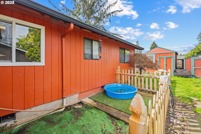 view of side of home featuring an outdoor structure, fence, board and batten siding, and a storage unit