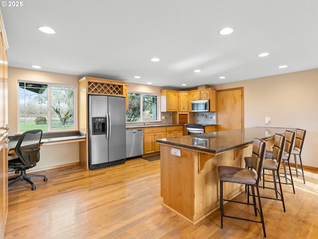 kitchen featuring light wood finished floors, baseboards, appliances with stainless steel finishes, and a breakfast bar