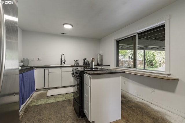 kitchen featuring white cabinets, a sink, dark countertops, black / electric stove, and stainless steel refrigerator