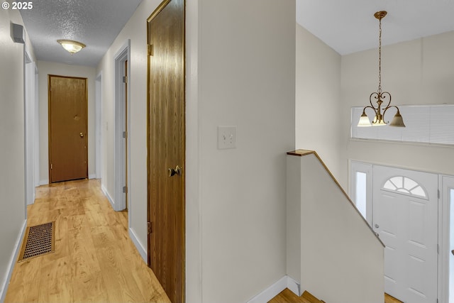 foyer with a textured ceiling, light wood-style flooring, visible vents, baseboards, and an inviting chandelier