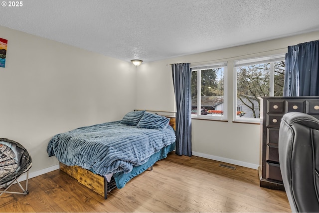 bedroom with visible vents, a textured ceiling, baseboards, and wood finished floors