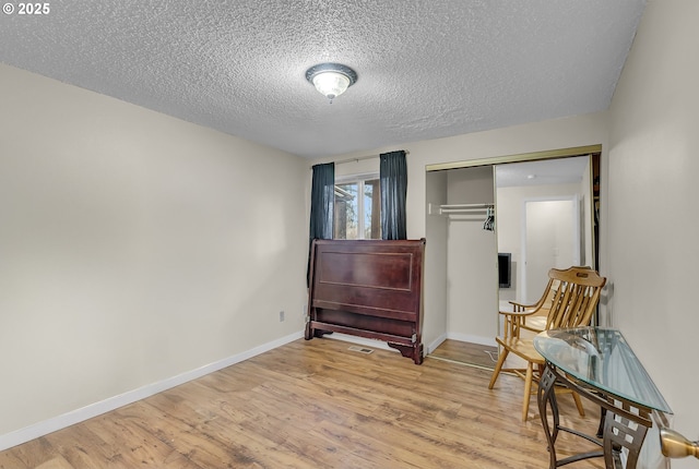 bedroom with a closet, light wood-style flooring, baseboards, and a textured ceiling