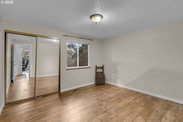 unfurnished bedroom with light wood-type flooring, a textured ceiling, baseboards, and a closet