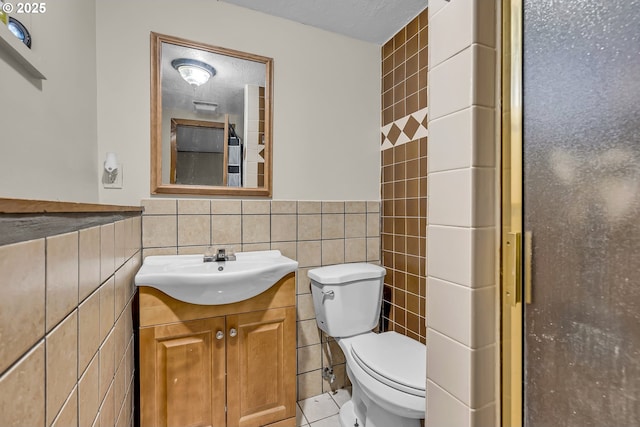 bathroom with a shower with door, tile walls, toilet, wainscoting, and vanity