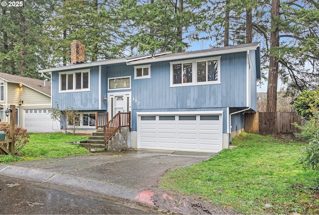 raised ranch with aphalt driveway, a chimney, an attached garage, a front yard, and fence