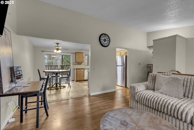 living room featuring lofted ceiling, a textured ceiling, light wood-type flooring, and baseboards