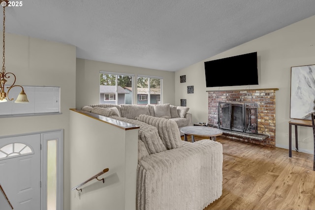 living area featuring vaulted ceiling, a textured ceiling, a fireplace, and light wood-style floors