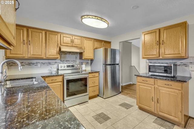 kitchen featuring stainless steel appliances, a sink, under cabinet range hood, and dark stone countertops