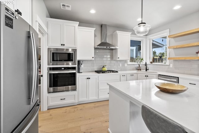 3588 Nestucca Loop, Eugene, OR 97408 - kitchen featuring stainless steel appliances, wall chimney range hood, light wood-style flooring, decorative backsplash, and white cabinets