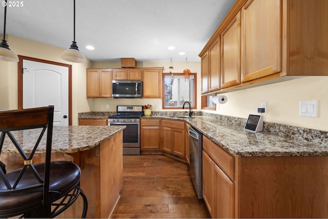 kitchen with a breakfast bar area, appliances with stainless steel finishes, dark wood-style flooring, stone counters, and a sink