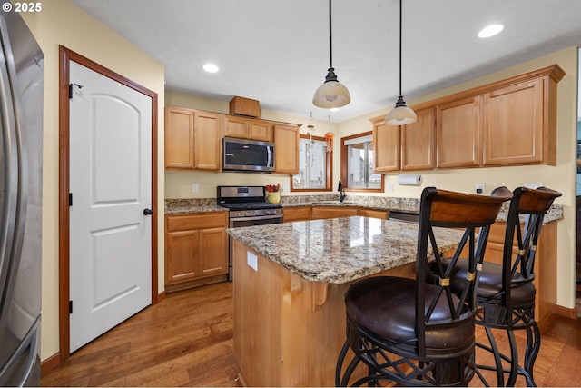 kitchen featuring dark wood-style floors, appliances with stainless steel finishes, light stone counters, and a center island