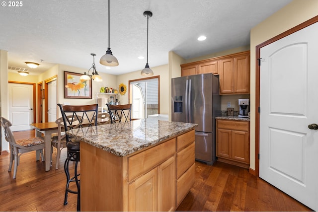 kitchen featuring dark wood-style floors, a center island, stainless steel refrigerator with ice dispenser, and light stone counters