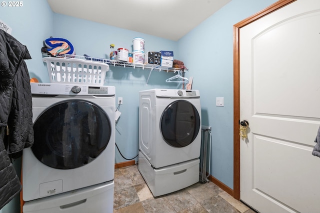 clothes washing area with laundry area, stone finish floor, washing machine and dryer, and baseboards