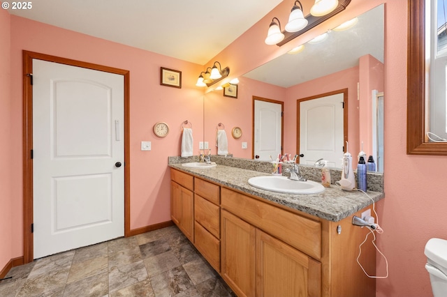 full bathroom with double vanity, baseboards, toilet, and a sink