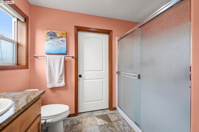 bathroom featuring toilet, a stall shower, stone finish floor, vanity, and baseboards