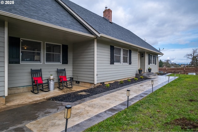 view of side of home with roof with shingles, a chimney, a lawn, entry steps, and a patio area