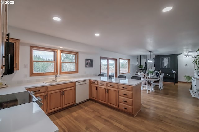 kitchen featuring a peninsula, a sink, light countertops, dishwasher, and pendant lighting