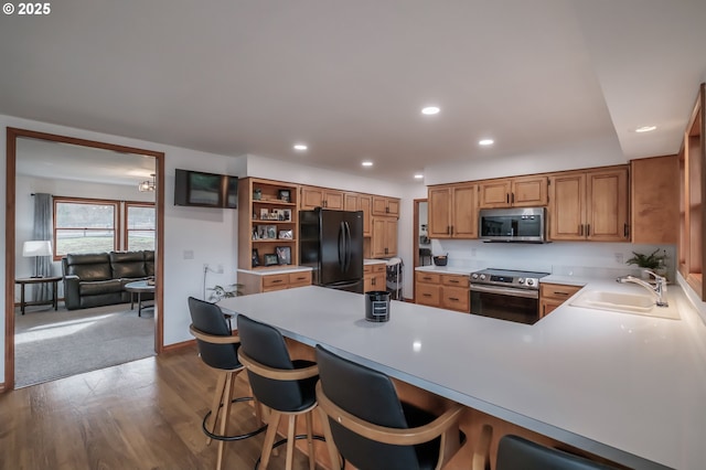 kitchen with recessed lighting, a sink, light countertops, appliances with stainless steel finishes, and brown cabinetry