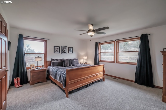 bedroom featuring a ceiling fan, multiple windows, light carpet, and baseboards