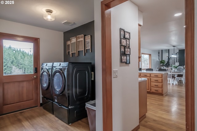 laundry area with light wood-type flooring, laundry area, washing machine and dryer, and plenty of natural light