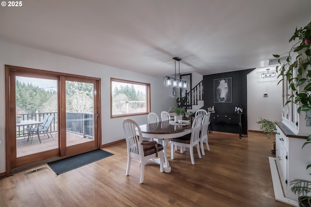 dining space with a notable chandelier, stairs, visible vents, and wood finished floors