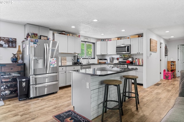 22165 SE Mark Rd, Damascus, OR 97089 - kitchen featuring appliances with stainless steel finishes, a sink, a textured ceiling, light wood-type flooring, and a kitchen bar