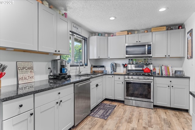 22165 SE Mark Rd, Damascus, OR 97089 - kitchen featuring stainless steel appliances, a sink, a textured ceiling, dark stone countertops, and light wood-style flooring