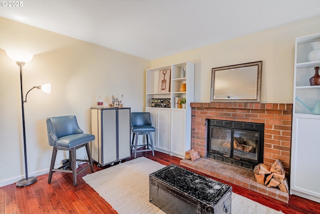 sitting room with hardwood / wood-style floors, a brick fireplace, built in shelves, and baseboards