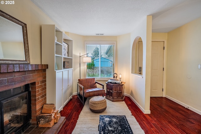 sitting room featuring wood finished floors, baseboards, visible vents, a fireplace, and a textured ceiling