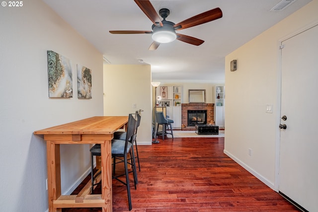 dining room with a brick fireplace, wood finished floors, visible vents, and baseboards