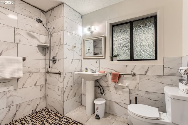 bathroom featuring toilet, a textured ceiling, tile walls, and a tile shower